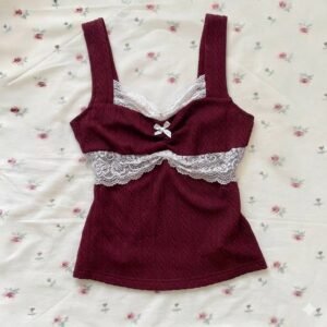 A deep burgundy cable-knit sleeveless top featuring white lace trim on the neckline and bust, accented with a small white bow, displayed on a floral rose-print background