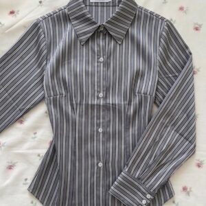 A grey and white vertical striped long-sleeve fitted button-down shirt with a pointed collar, laid flat on a floral rose-print background